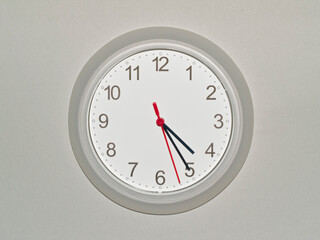 eine Wanduhr auf grauem Hintergrund zeigt die Zeit 04:25 Uhr