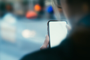 Cropped back view of young woman holding modern smartphone with blank screen area for your internet...