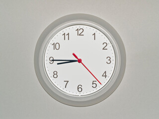 eine Wanduhr auf grauem Hintergrund zeigt die Zeit 08:45 Uhr