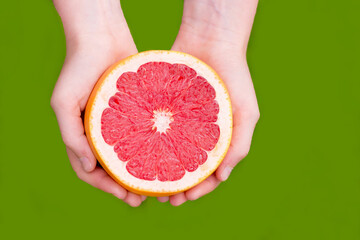 female hand holding a grapefruit  isolated on green