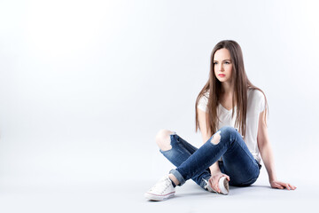 Fototapeta na wymiar Beautiful woman in a white t-shirt and jeans sits on the floor in studio.