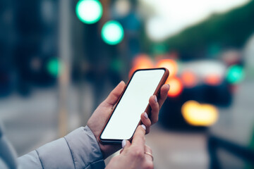 Cropped view of female hands holding modern smartphone device with copy space area for your internet website on bokeh background.Digital telephone with blank screen for your website