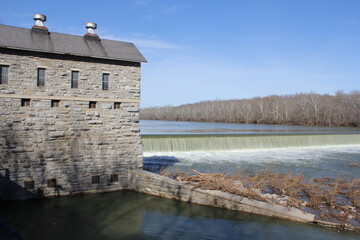 Fototapeta premium small old hydroelectric dam on a river with beautiful bright blue sky and trees in th ebackground