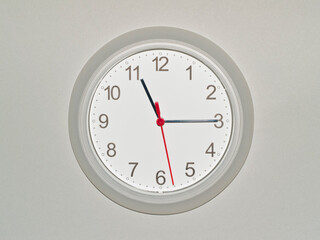 eine Wanduhr auf grauem Hintergrund zeigt die Zeit 11:15 Uhr