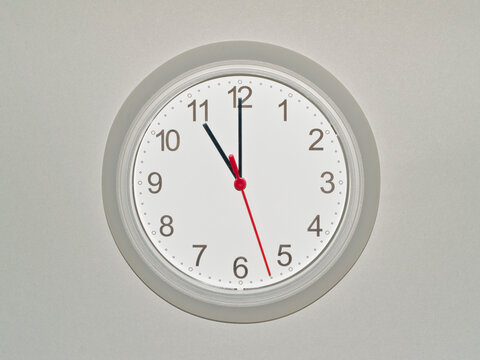 eine Wanduhr auf grauem Hintergrund zeigt die Zeit 11:00 Uhr