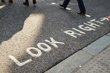 White look right warning sign in writing on the asphalt with feet of pedestrians crossing at sunset in London.
