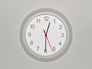 eine Wanduhr auf grauem Hintergrund zeigt die Zeit 12:30 Uhr