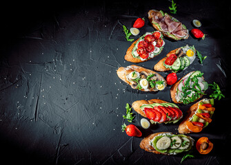Traditional italian bruschetta on toasted slices of baguette seasoned with spice and herbs and garnished with fresh basil on a dark background