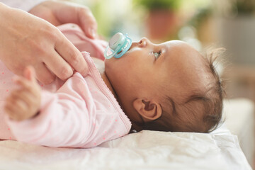 Side view close up of cute African-American baby sucking on pacifier while lying on changing table...