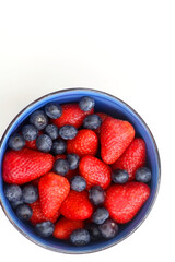 Bowl of blueberries and strawberries on white background. Top view.