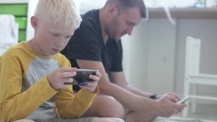 Dad and son play games on the mobile phone at home on the floor. Focus on the baby, the man in the background is blurred. - Powered by Adobe