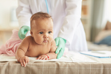 Portrait of cute African-American baby lying on belly at changing table during checkup at doctors office, copy space