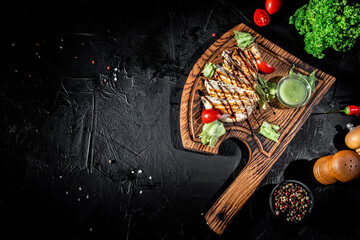 Grilled chicken fillets with herbs and spices served on wooden cutting board on dark background
