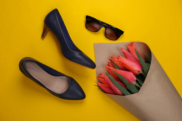 Bouquet of tulips, high-heeled shoes with sunglasses on a yellow background. Top view. Flat lay