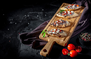Bruschetta with tomatoes, mozzarella cheese and basil on dark background. Traditional italian appetizer or snack, antipasto
