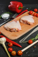 chicken thighs in a wooden Cutting board, fresh rosemary, fresh cherry tomatoes, fresh chili peppers, garlic, lime and sea salt on a black background.