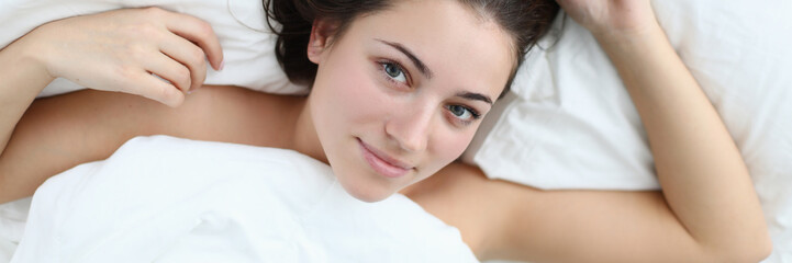 Close-up of wonderful woman after waking up looking at camera with gladness and smile. Beautiful lady relaxing in bedstead after wakeup. Relaxation and vacation concept