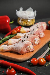 Chicken Leg in a wooden Cutting board, fresh rosemary, fresh cherry tomatoes, fresh chili peppers, garlic, lime and sea salt on a black background.