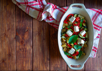 Obraz na płótnie Canvas Ratatouille, backed vegetable with feta cheese and fresh basil in white oven pan on wooden brown background with copy space.
