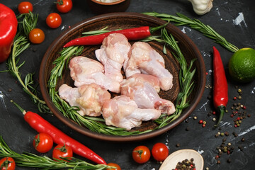 chicken legs in a in in a clay plate, fresh rosemary, fresh cherry tomatoes, fresh chili peppers, garlic, lime and sea salt on a black background.