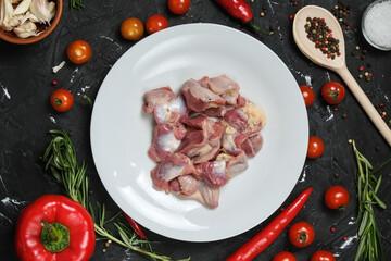 Chicken ventricles in a in a white plate, fresh rosemary, fresh cherry tomatoes, fresh chili peppers, garlic, lime and sea salt on a black background.