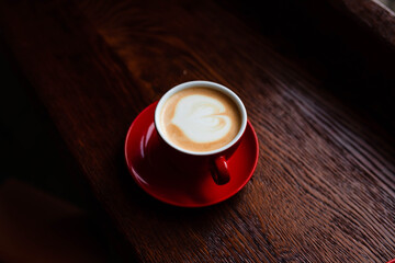 Hot coffee with latte art in a white cup with saucers on a wooden table. Cappuccino with foam. Cup of coffee on a wooden table. Top view. Place for text. Cappuccino with latte.