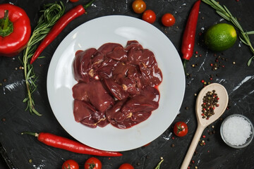 Chicken ventricles in a in a white plate, fresh rosemary, fresh cherry tomatoes, fresh chili peppers, garlic, lime and sea salt on a black background.
