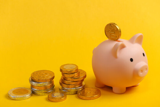 Piggy bank with coins on yellow background.