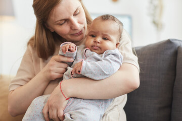 Portrait of mature Caucasian woman holding cute mixed-race baby while enjoying motherhood at home, copy space