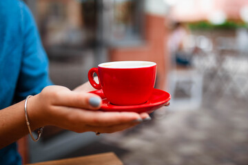 Cup of cappuccino in the hands of a young girl. Girl holding a red cup with coffee on a wooden background, hand plan and coffee. Top view. Place for text. Cappuccino with latte.
