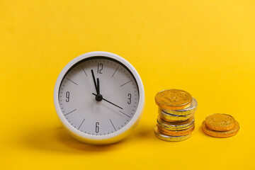 Time is money. White clock with a stack of coins on yellow background