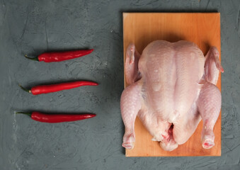 Raw whole chicken with chili peppers on a wooden board on a light background