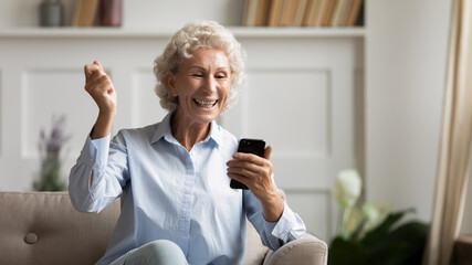 55s woman sit on sofa holding smartphone feels very happy by received news sms notice. New application older generation easy convenient usage, e-store sales incredible luck on-line lottery win concept
