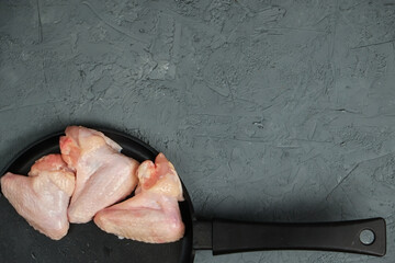 Raw Chicken legs in a in a frying pan on a blackboard on a light background