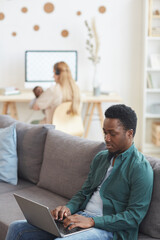 Vertical portrait of modern interracial family working from home, focus on African-American man using laptop in foreground, copy space