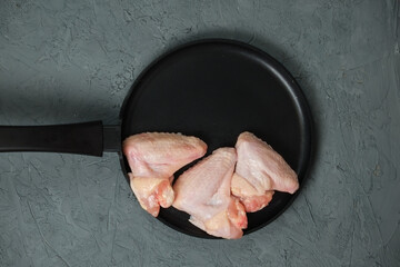 Raw Chicken legs in a in a frying pan on a blackboard on a light background