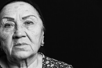 Black and white portrait on an old woman on a black backgound. Sad grandmother