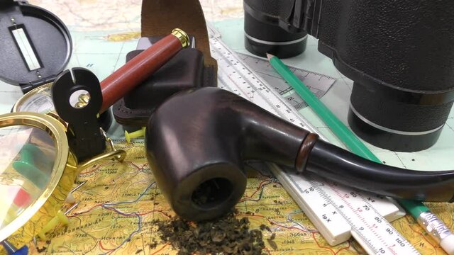 A magnetic compass, where it is used as a navigation tool, and a map are necessary for building a route or orientation, and a tobacco pipe with tobacco reminds of past adventures.