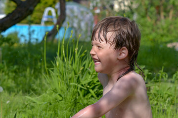Naklejka na ściany i meble a small boy plays in the water on the lawn in front of a country house 