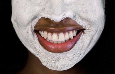 Naklejka premium Facial treatment, mud clay cleansing mask. Cropped close up image of half of face of beautiful African woman with white clay facial mask on face. Nice smile of charming woman with facial mask