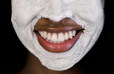 Facial treatment, mud clay cleansing mask. Cropped close up image of half of face of beautiful African woman with white clay facial mask on face. Nice smile of charming woman with facial mask