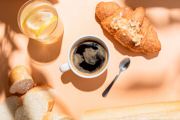 top view of coffee, water, baguette and croissant for breakfast on beige table