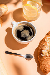 coffee, water and croissant for breakfast on beige table