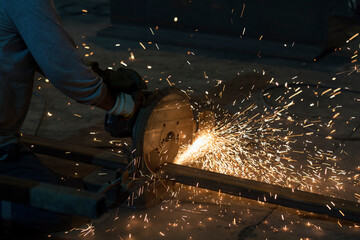 The metal worker is cutting a steel material with circular saw machine and sparks. A circular saw is a tool for cutting many materials such as wood, masonry, plastic or metal and may be hand-held.