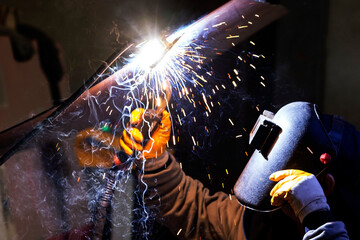 The welder is welding to a steel plate. Welding is the process of joining two plastic or metal parts by melting them with or without using a further molten material.