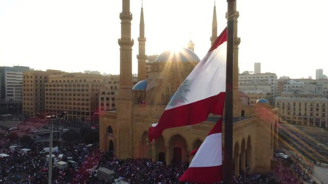 Beirut, Lebanon 2019 : sunset drone shot ped up on Lebanese flag in martyrs square with church and mosque and sun flaring in the background during the Lebanese revolution 