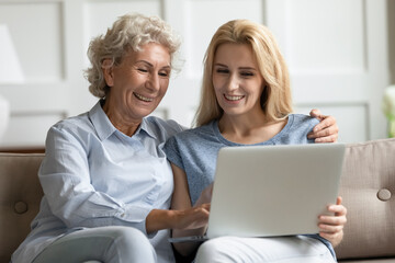 Adult daughter helps to elderly mother with notebook usage, explains teaches older relative how to use device. Family having fun watching movie on computer, buying via internet, store services concept