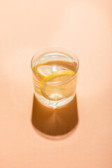 glass of fresh water with lemon slices on beige with shadow