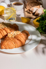 fresh croissants, bread, coffee and lemon water for breakfast on grey table, selective focus