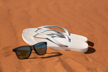 Gafas de sol y chanclas en arena del desierto.